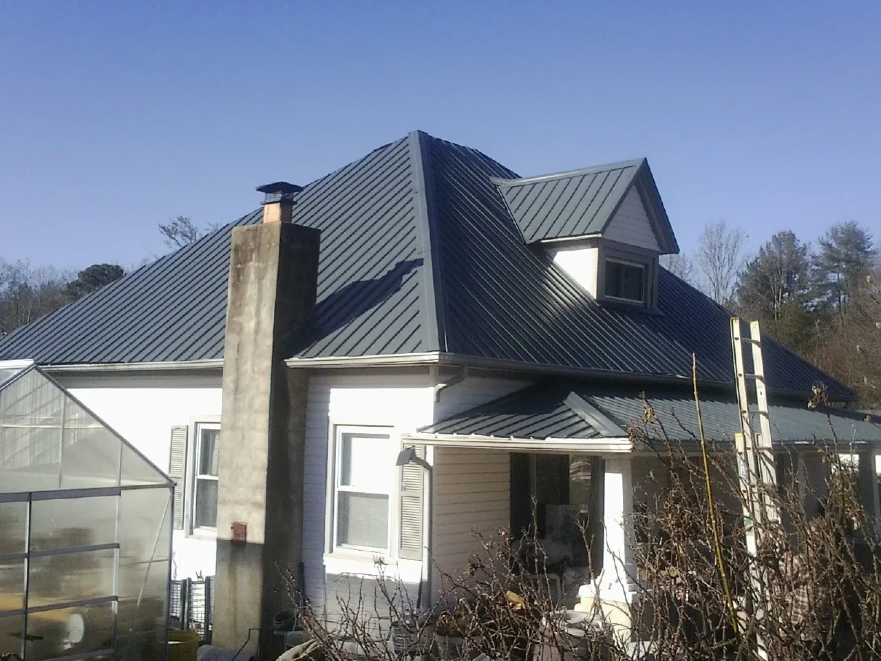 Dark blue standing seam metal roof on a white farmhouse with dormer — Slate & Tile Roof Repair by Roofing Brothers in Brilliant