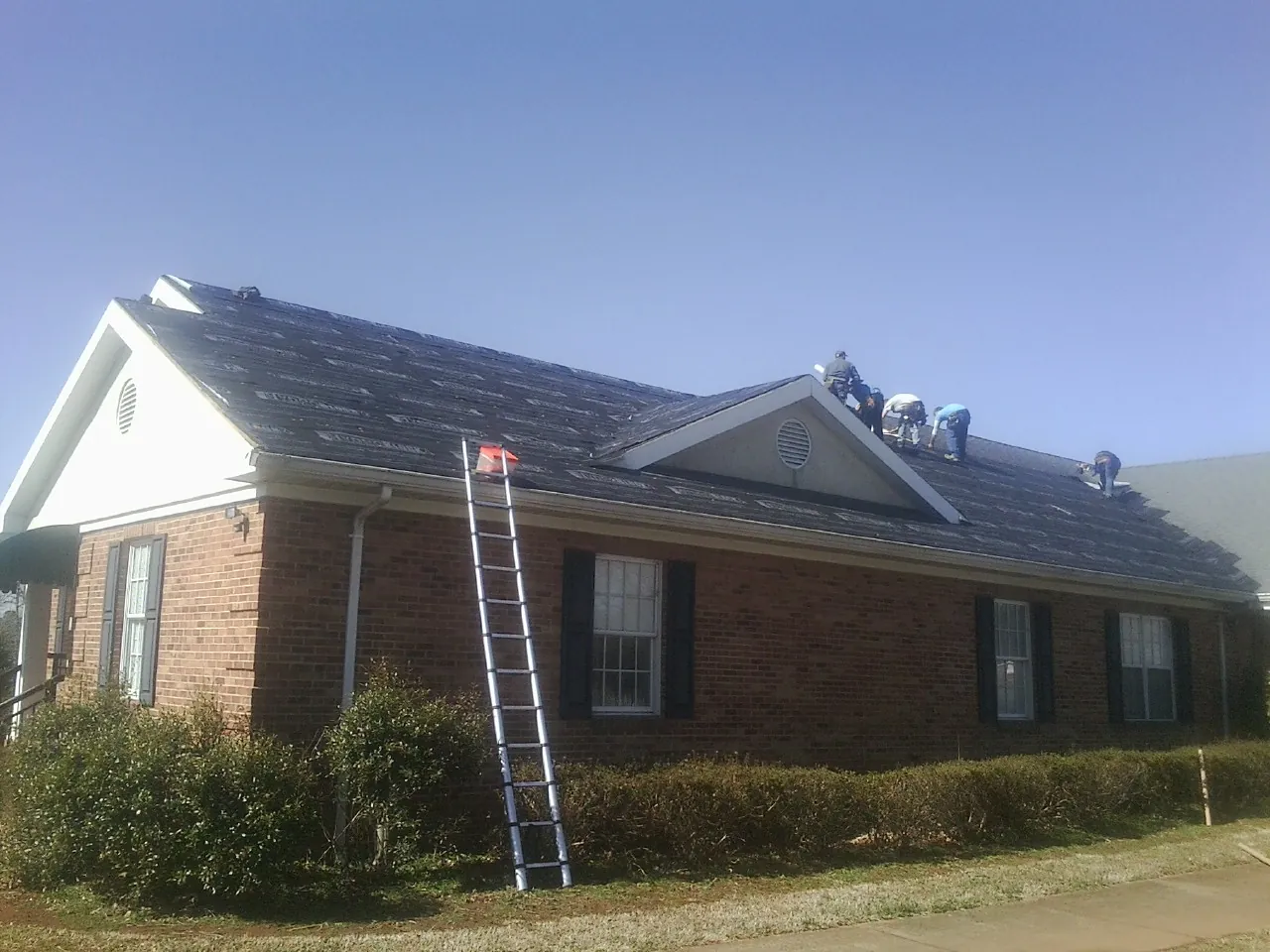 Crew tearing shingles off a brick ranch roof with a ladder set — Emergency Roof Repair work by our crew in Brilliant