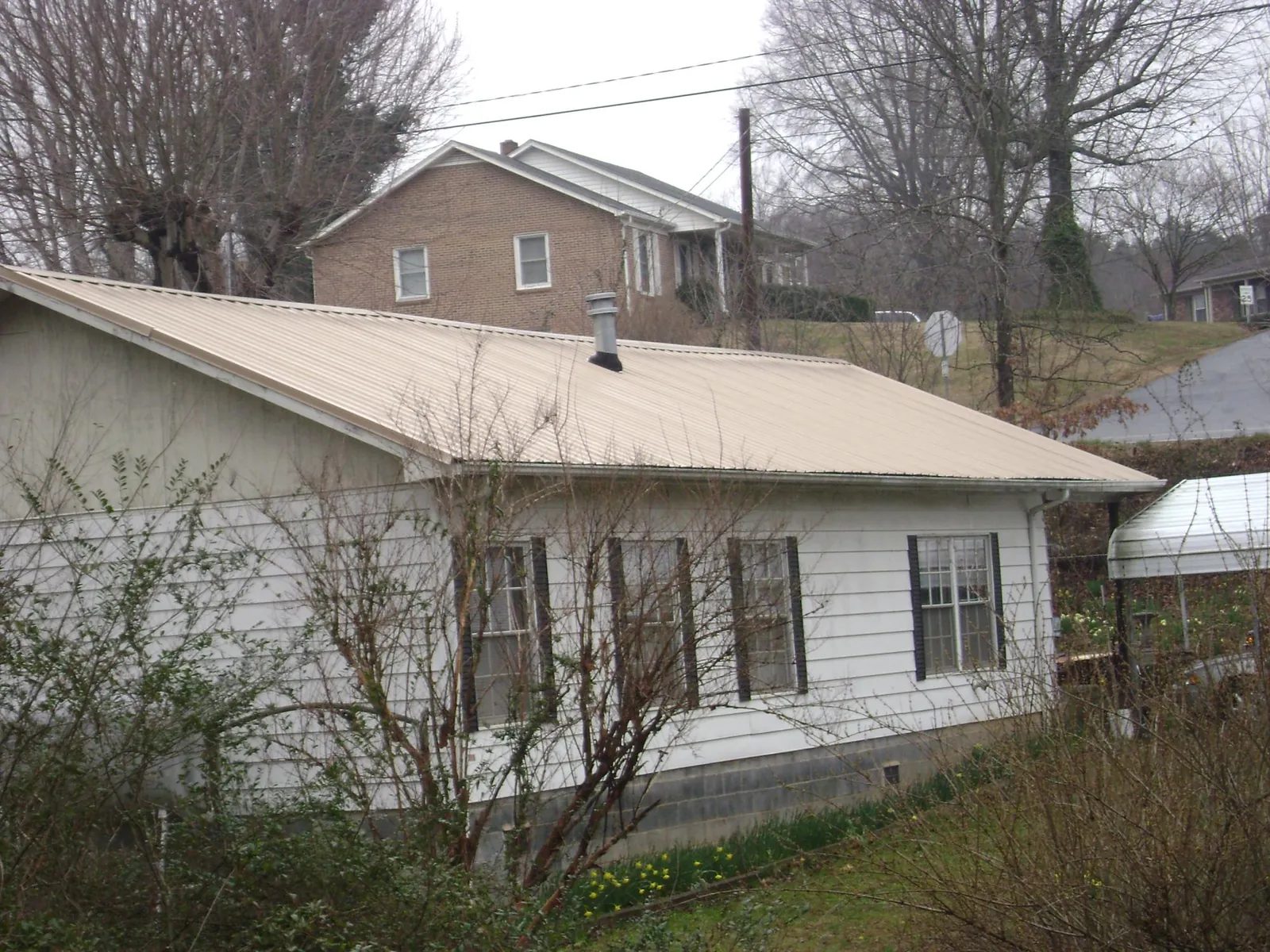 Tan metal roof on a white sided house set into a hillside — Commercial Roofing by Roofing Brothers in Brilliant